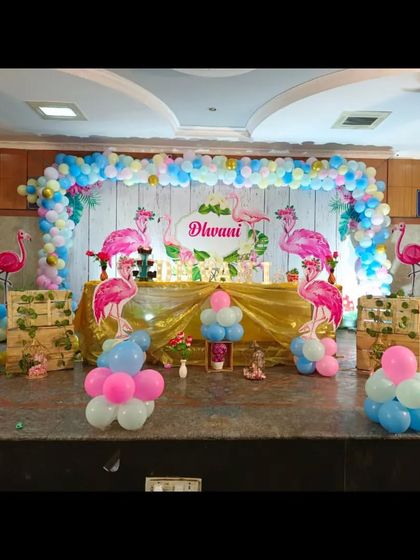 This is a tropical flamingo themed birthday party I put together. The stage includes a large balloon arch, flamingo cutouts, and themed props set against a rustic wooden panel backdrop.