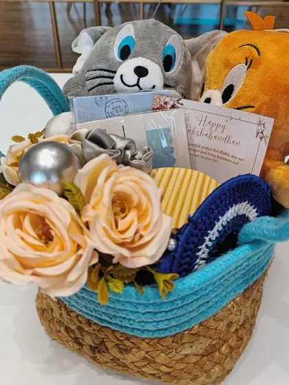 This view of the Tom and Jerry hamper shows the full curation in a woven basket. It includes plushies, a Rakhi card, a scented candle, and other small gifts, perfect for celebrating the crazy bond between siblings.