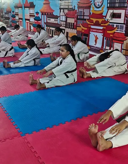 A class of black-belt and senior students performing seated forward-fold stretches to improve their flexibility and recovery.