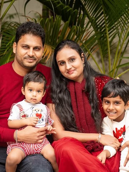 A beautiful family of four posing for an outdoor portrait. The coordinated red outfits create a warm and cohesive look against the natural green background.