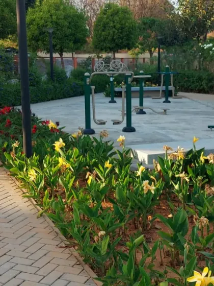 An outdoor gym area in a public park, surrounded by neat flower beds and a brick pathway. The landscaping enhances the recreational space, making it more enjoyable.