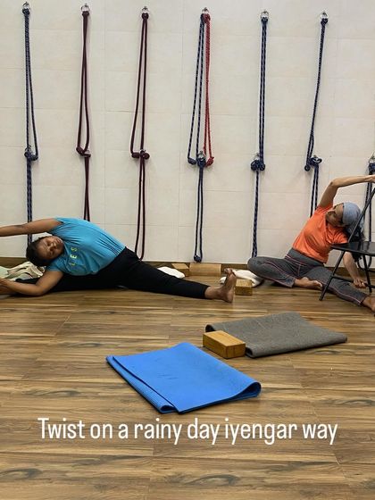 Students practicing seated twists on a rainy day. One student uses a chair for support, showing how asanas can be adapted for different needs.
