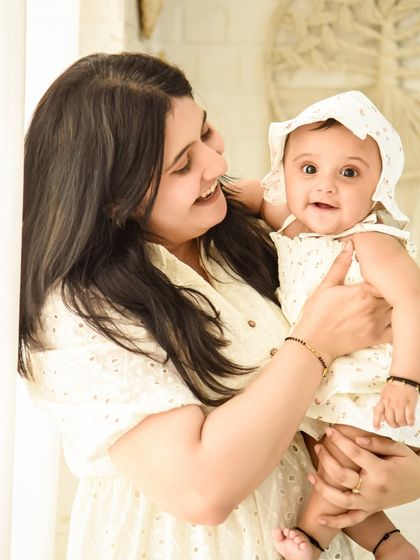 A mother holds her smiling six-month-old baby, who is wearing an adorable bonnet. This portrait celebrates the half-birthday milestone with a simple and sweet setup.