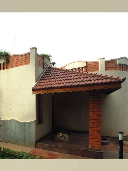 A small porch with a tiled roof and brick pillar, attached to a building with curved, plastered walls.