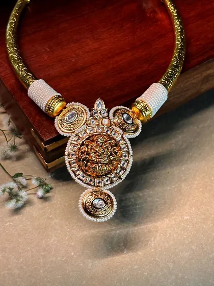 A magnificent temple-style hasli bracelet, featuring a central deity motif surrounded by polki and pearls.