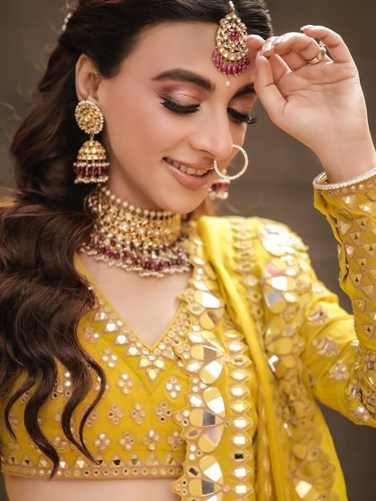 A delicate close-up of the bride, her hand gently touching her maang tikka, highlighting her beautiful jewelry and makeup.