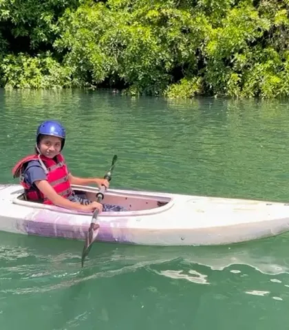 A young girl in a kayak pauses to smile for the camera, with the clear green water of the Kali River around her.