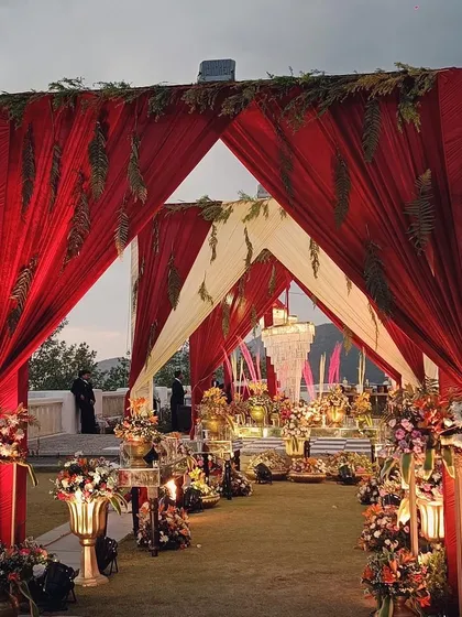 A grand entrance for a mountain wedding, with canopies of red and white fabric leading to an area filled with traditional brass decor and floral arrangements.