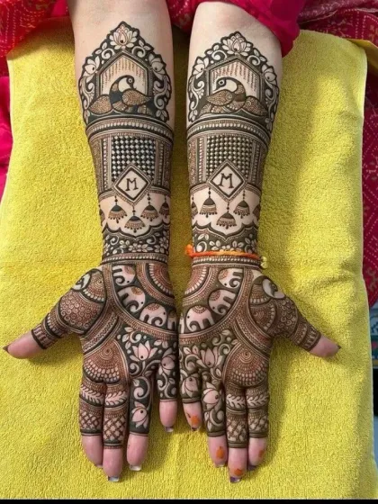 A symmetrical design featuring peacocks inside jharokhas on both arms. The palms have a dense pattern of elephants and lotuses, and the bride's initial 'M' is subtly included in the design.