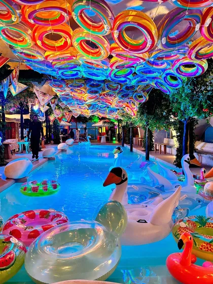 We transformed this space into a vibrant St. Tropez beach club, complete with a pool filled with colorful floats, swan inflatables, and a ceiling of rainbow-hued rings. This design captures the fun and luxury of a glamorous poolside soiree.