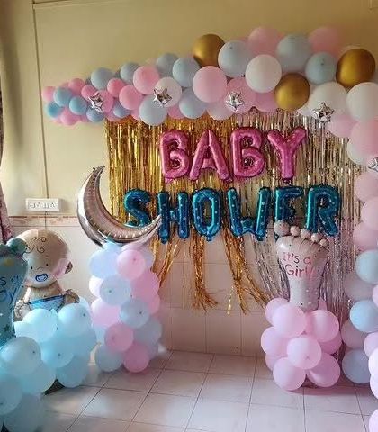 A similar baby shower setup for a home celebration, using pink, blue, and gold balloons to create a festive backdrop.