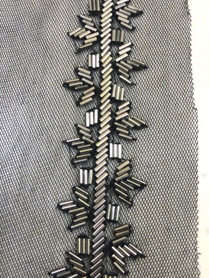 A close-up of a hand-beaded trim on a black net base. The geometric pattern is created with metallic bugle beads, offering a modern and sophisticated embellishment for gowns and western wear.