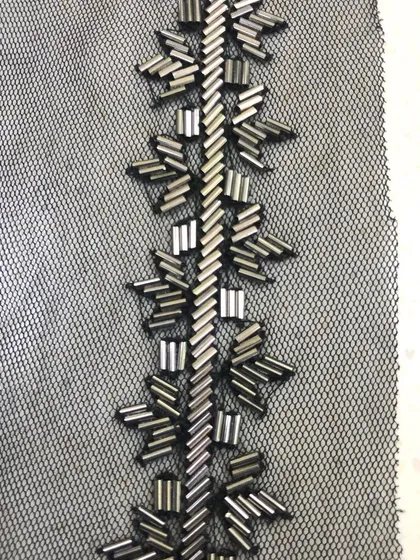 A close-up of a hand-beaded trim on a black net base. The geometric pattern is created with metallic bugle beads, offering a modern and sophisticated embellishment for gowns and western wear.