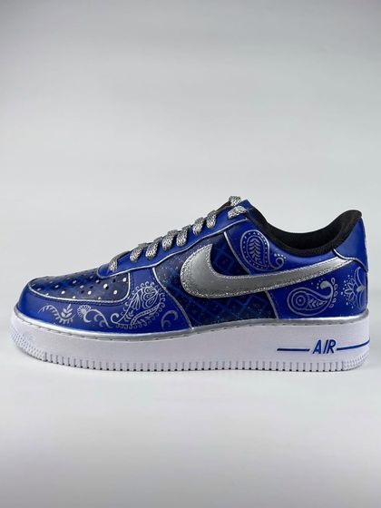A pair of royal blue custom Nike Air Force 1s with intricate silver paisley designs, created for a wedding carnival.