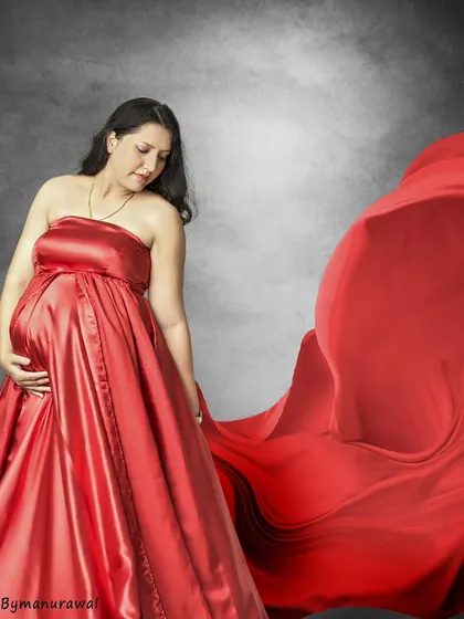 A classic studio shot featuring a flowing red gown. The movement in the fabric adds a touch of drama, while the mother's gentle gaze towards her bump creates a feeling of quiet connection.