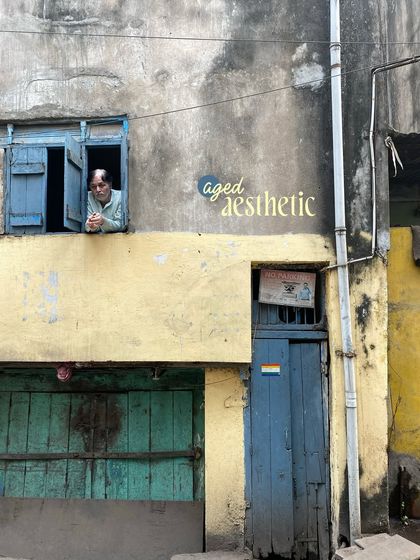 An 'aged aesthetic' indeed. An elderly man looks out from his window with its bright blue shutters, above a weathered green and blue facade.