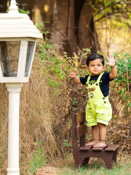 A playful wave from this little one during his outdoor park photoshoot. The lamppost prop adds a classic, charming element to the natural scenery.