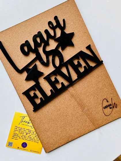 The "Laavi is Eleven" black acrylic topper, presented on its sturdy cardboard backing, ready for shipping.