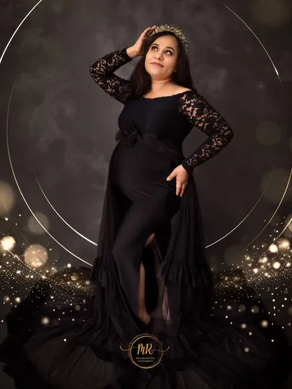 A chic and stylish maternity photo. The mother-to-be poses in a black gown and crown, with sparkling bokeh effects and a golden ring of light adding a touch of glamour.