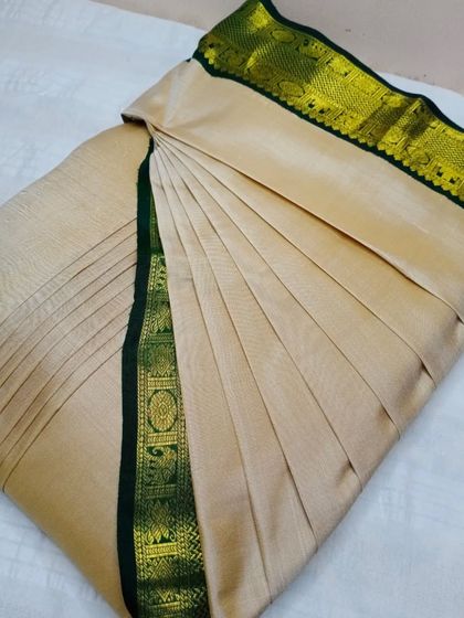 An elegant beige saree with a green and gold border. The pleats are customized to ensure a sleek and flattering drape.