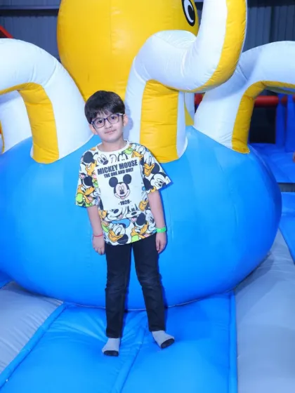 A young boy stands proudly in front of a giant inflatable octopus. Our play structures are designed to spark imagination and adventure.