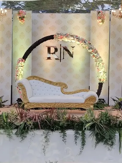 A scintillating reception stage with a circular floral arch for the couple's monogram, flanked by modern candle stands and lush greenery.