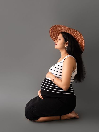 An artistic and serene portrait of a mom-to-be kneeling in profile, wearing a hat for a touch of style.