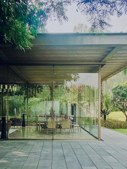 This lightweight steel and glass pavilion sits beside a pool in Delhi. The design prioritizes transparency and a connection to the garden, using a perforated jaali roof to filter sunlight and create a gentle, shaded atmosphere.