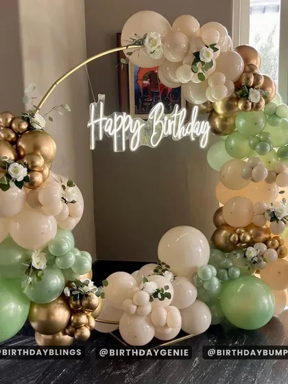A beautiful and organic-feeling balloon arch on a gold ring frame. The colors of sage green, cream, and gold, along with white floral sprigs, create a fresh and elegant look.