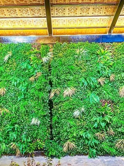 Two large panels of mixed tropical foliage create a stunning backdrop. The lighting from above highlights the different leaf textures, adding depth and drama to the installation.