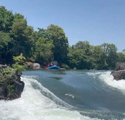 A beautiful, wide shot of a raft heading towards a natural slide rapid in Dandeli, surrounded by rocks and trees.