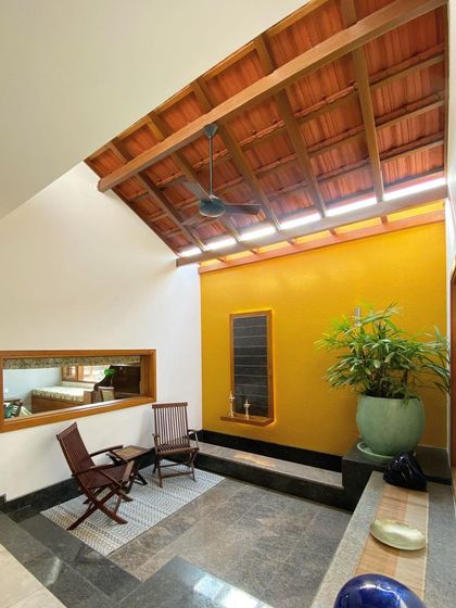 This cozy, semi-outdoor seating area is sheltered by a traditional tiled roof with a skylight. The combination of a vibrant yellow wall and natural stone flooring creates a warm and rustic spot to relax.