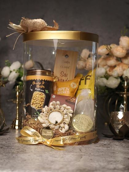 A clear cylinder hamper is a modern way to present Diwali gifts. This one is filled with festive snacks and a shell-adorned T-light holder, all tied together with a custom ribbon.