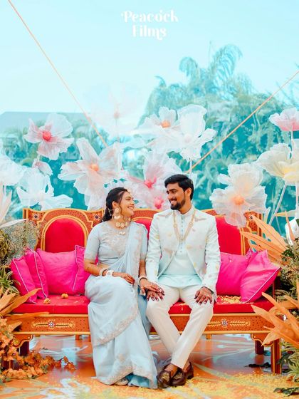 A colorful and happy portrait of the couple seated on a bright red sofa during their Haldi event, surrounded by whimsical floral decor.