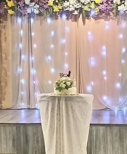 A close up of the wedding cake on stage, with fairy lights creating a magical backdrop.
