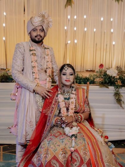A classic portrait of the couple seated, their regal attire and the grand decor creating a timeless wedding photograph.