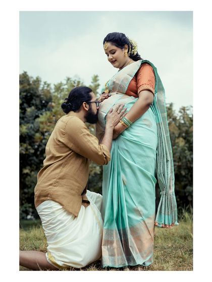 A touching photo from a traditional baby shower, where the father-to-be kneels to kiss his wife's belly. This image beautifully captures a gesture of love and blessing for their unborn child.