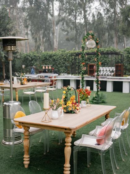 A tablescape from the autumn-themed brunch, with a simple wooden table, ghost chairs, and a centerpiece of warm-toned florals.