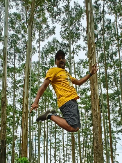 A traveler jumping for joy in the pine forests of Kodaikanal. The tall trees and quiet atmosphere are rejuvenating.