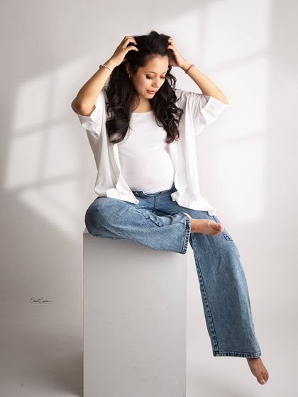 A relaxed and stylish pose. This mom-to-be looks effortlessly cool in her jeans and white shirt, seated on a white block.