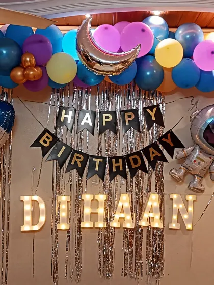 A space-themed birthday decoration set up at home. This features a silver tinsel curtain, a 'Happy Birthday' banner, marquee letters for the name, and astronaut-themed foil balloons.