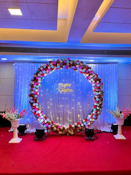 A simple yet stunning engagement ring decoration. This backdrop features a large floral ring, a "Better Together" neon sign, and a fairy light curtain, all set against a red carpet.