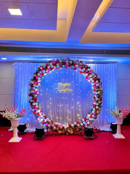 A simple yet stunning engagement ring decoration. This backdrop features a large floral ring, a "Better Together" neon sign, and a fairy light curtain, all set against a red carpet.