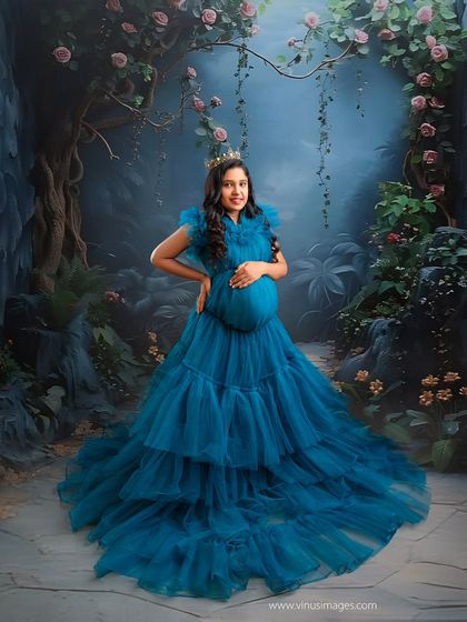 A fairytale forest scene. The mother-to-be, in a stunning tiered blue gown and crown, looks like a queen in an enchanted wood.