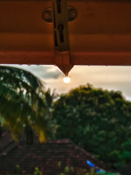 A wider view of the sun-in-a-droplet shot, showing more of the surrounding environment with the palm trees and village rooftops in the background.