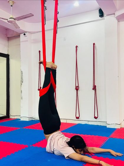 The hammock offers support for deep stretches that might be challenging on the mat. This student is using it to assist with a supported plow pose, gently stretching the spine and hamstrings.