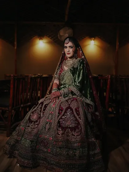 A regal, seated portrait of the bride in her magnificent wedding lehenga, showcasing the rich details and craftsmanship of her attire.