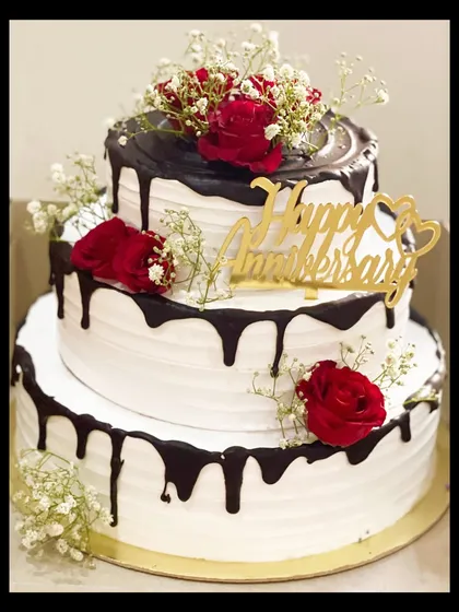 A grand 5kg, three-tier anniversary cake. This statement piece features a rich chocolate drip over white buttercream, adorned with fresh red roses and baby's breath.