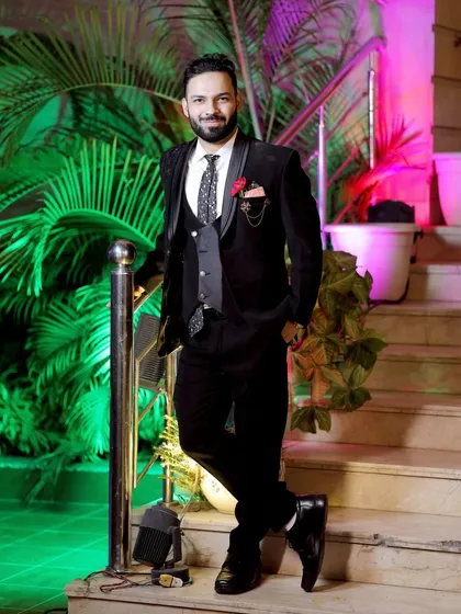 A stylish portrait of the groom leaning against a railing. The green background makes his black suit pop.