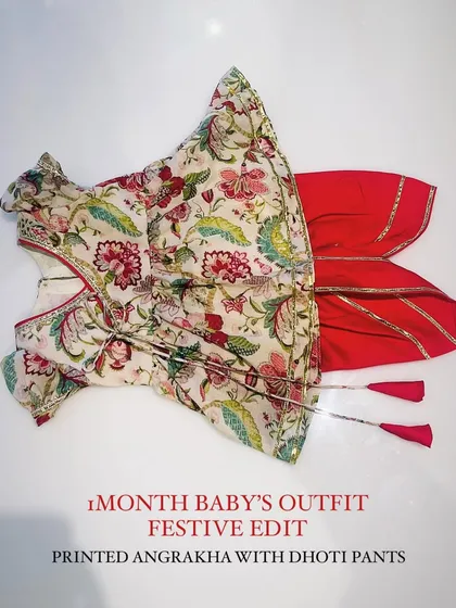 This complete festive set for a one-month-old baby includes a traditional floral print Angrakha top with tassel ties, paired with comfortable red dhoti pants finished with gota patti borders. It's designed for both style and comfort during family celebrations.